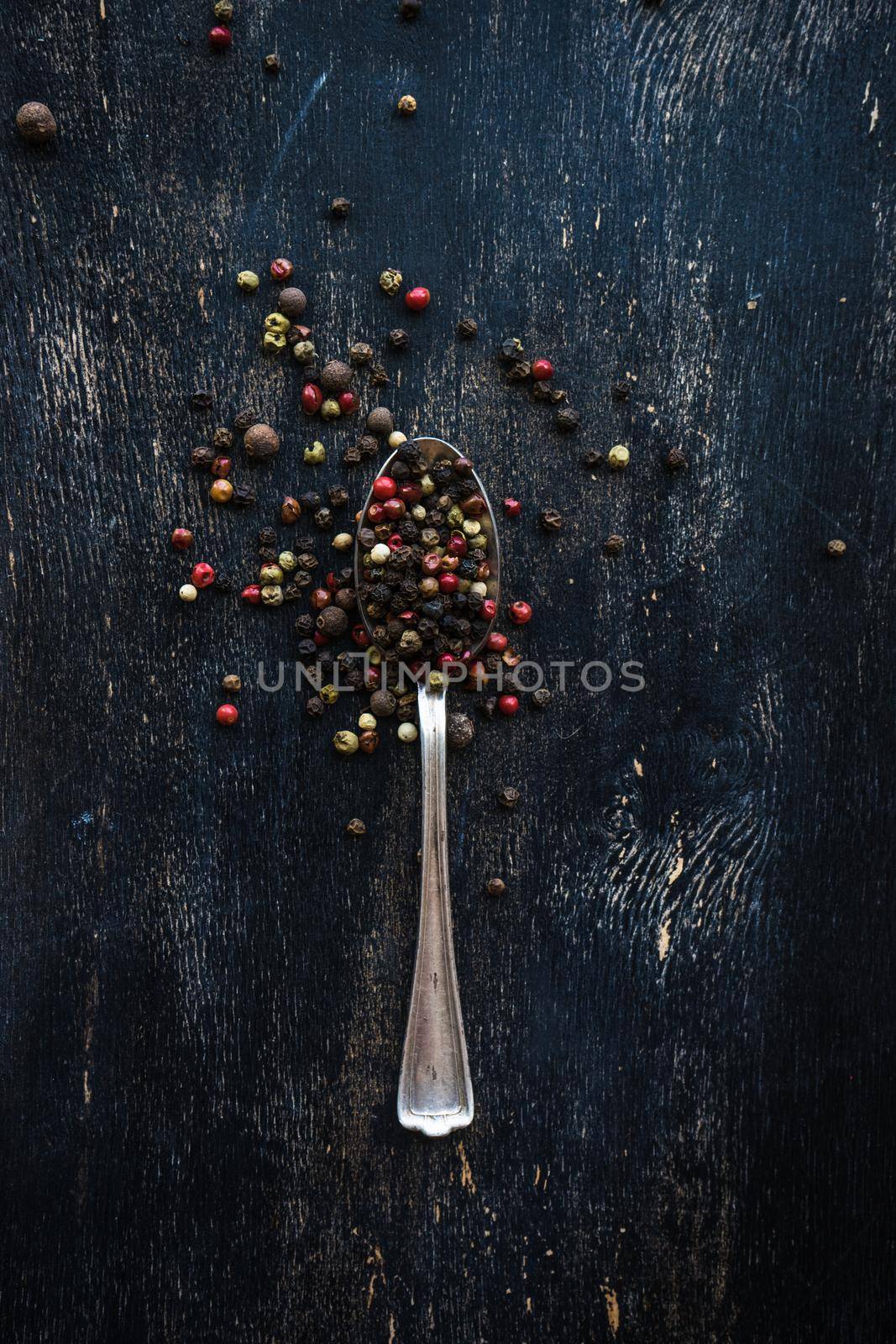 Vintage spoons with pepper on dark wooden background with copyspace