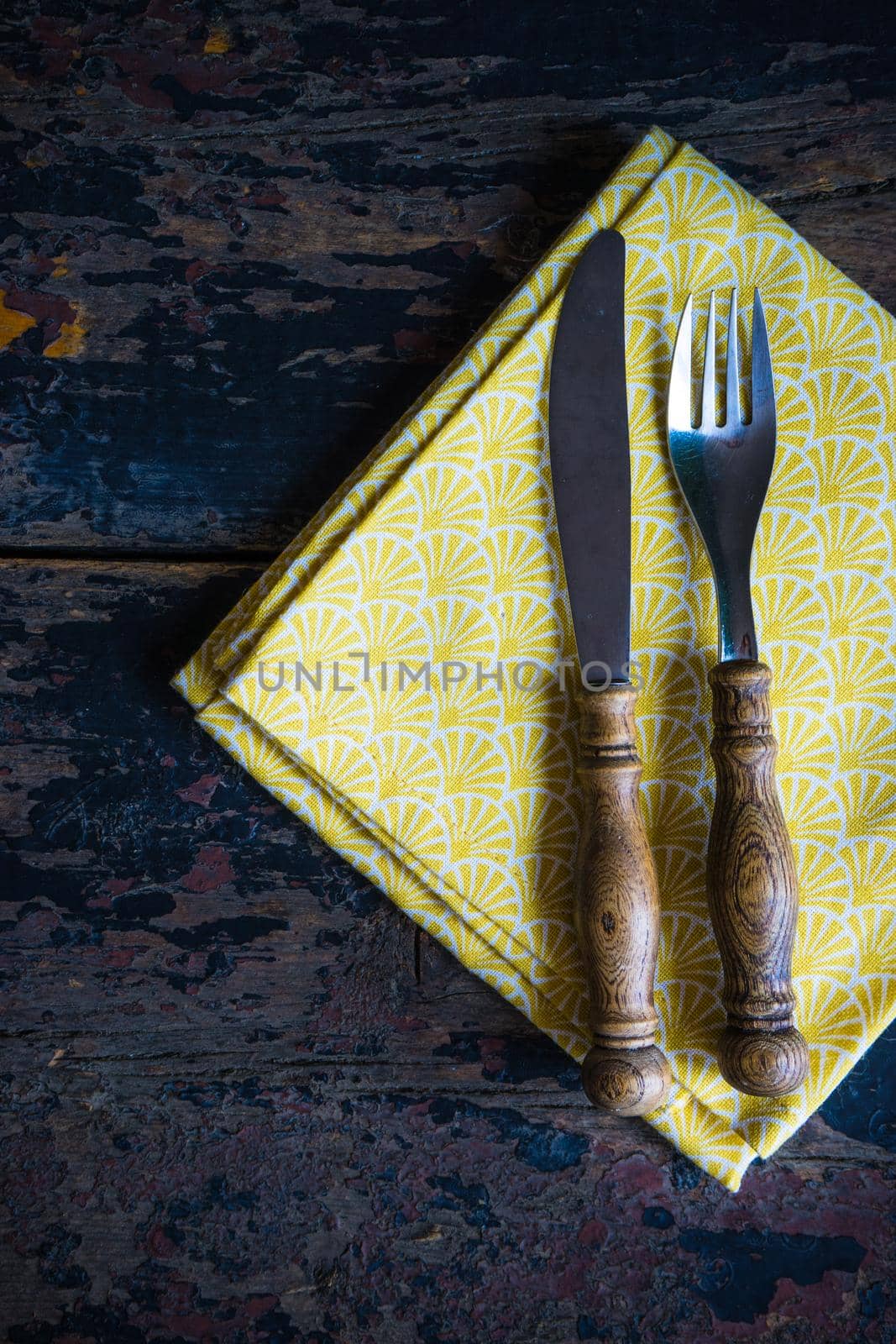 Rustic table setting with bright napkin nd silverware on dark wooden table