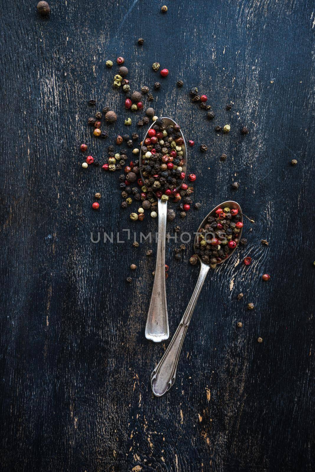 Vintage spoons with pepper on dark wooden background with copyspace