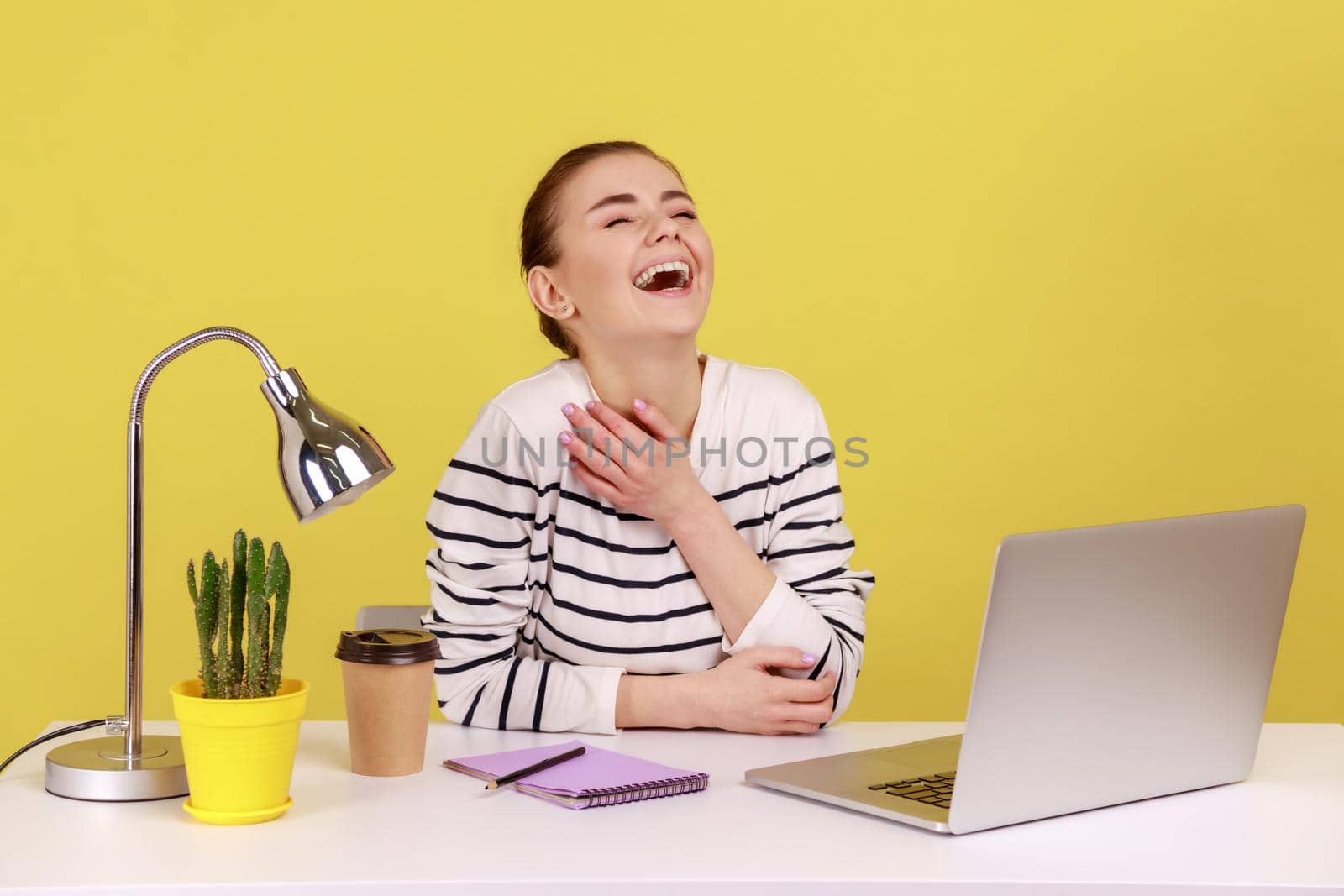 Amused happy woman employee laughing out loud, being hysterical at crazy joke on laptop, having break at workplace home office. Indoor studio studio shot isolated on yellow background.