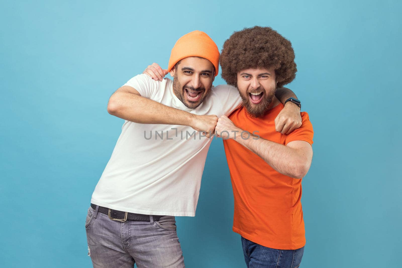 Yes we did. Portrait of two handsome happy excited young adult hipster men celebrating triumph together, showing bro fist, power five sign. Indoor studio shot isolated on blue background.