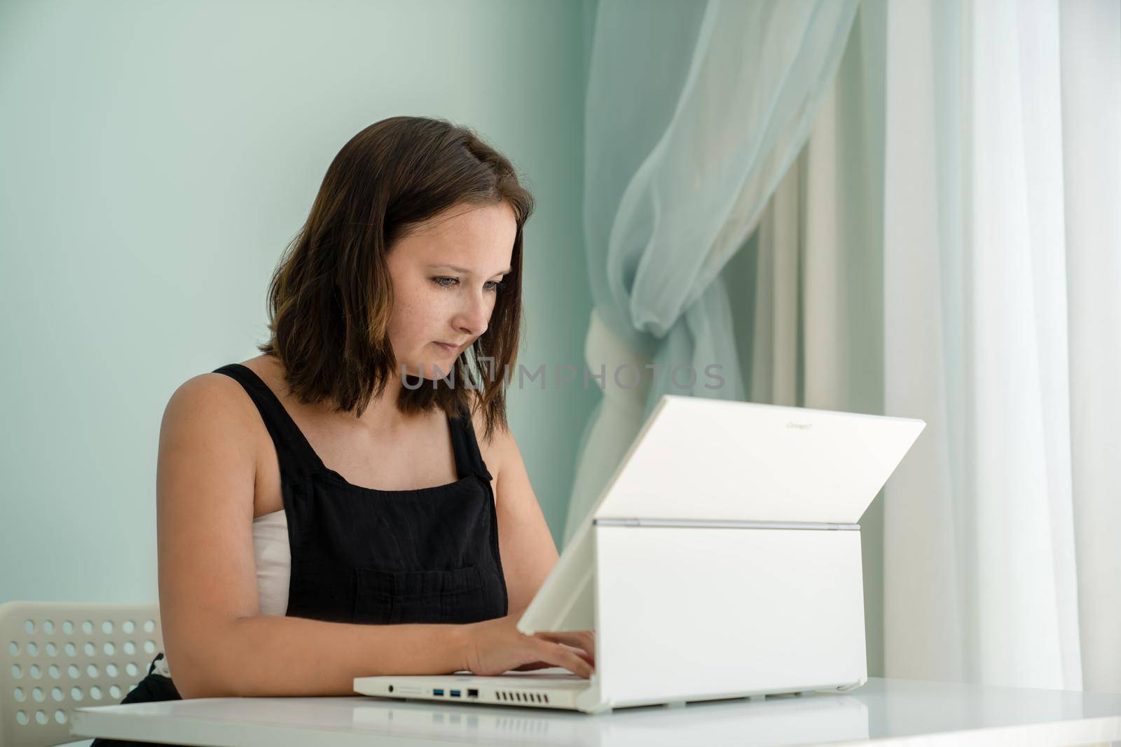 Girl is sitting in front of her laptop transformer at desk in her house. Concept of remote work and education, side view