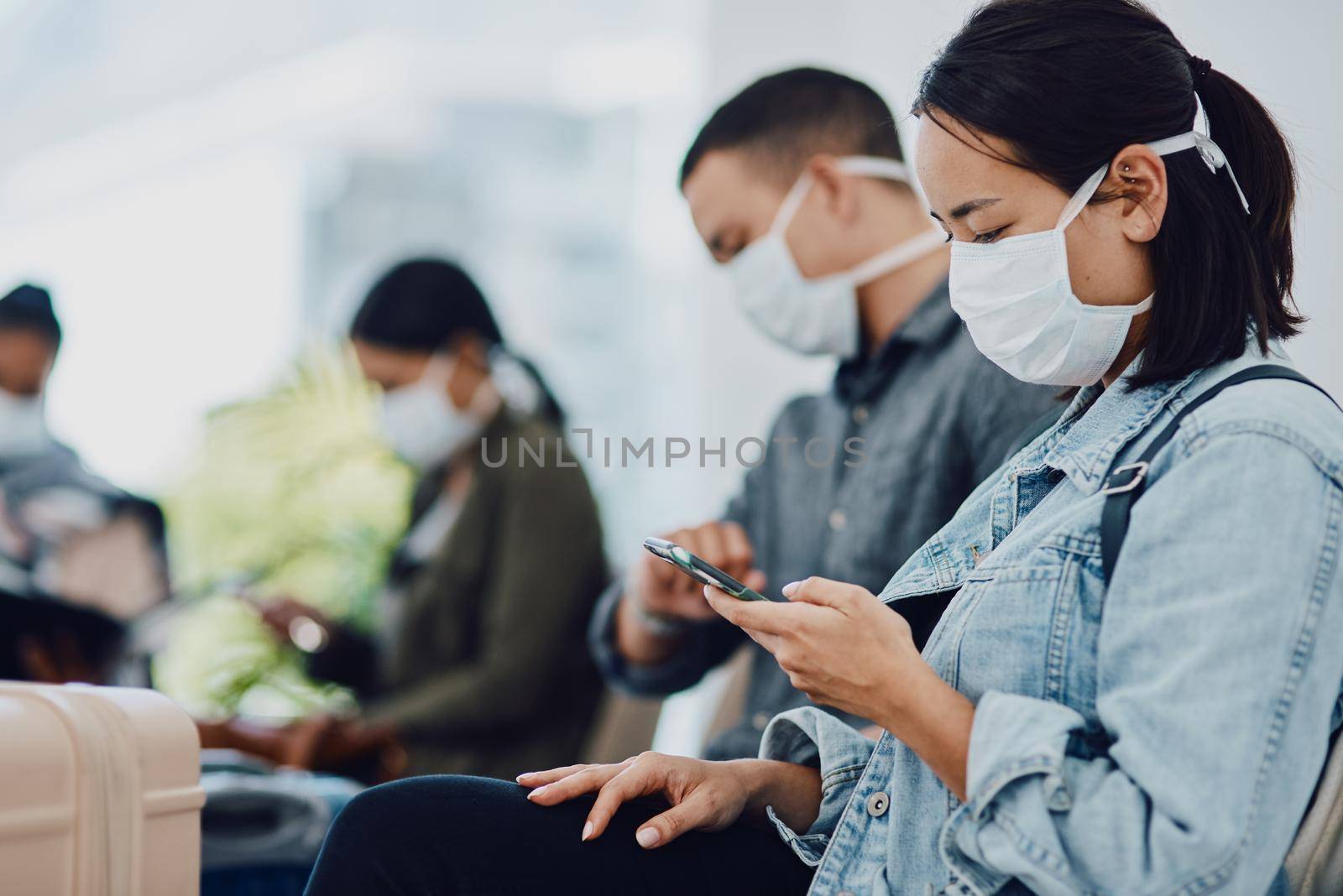 Female tourist on phone traveling during covid at airport waiting for departure, wearing a mask for protection. For hygiene and healthcare security, follow corona virus social distance regulations