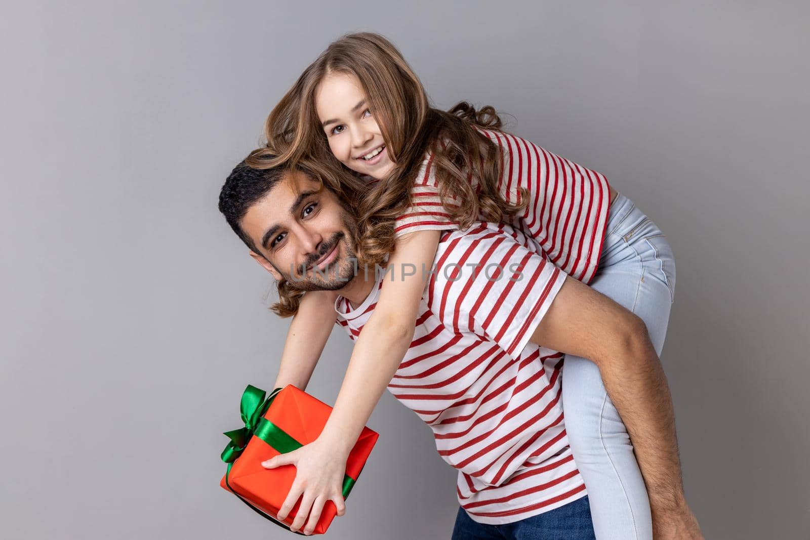 Father and daughter celebrating holiday together, dad holding kid with present box on his back. by Khosro1