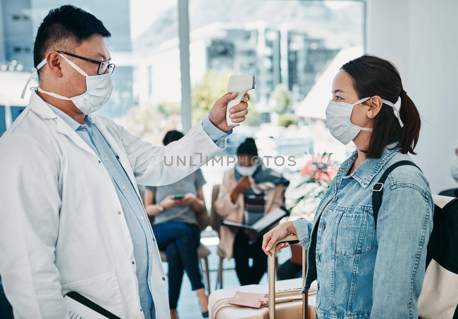 Covid traveling with a doctor taking temperature of a woman wearing a mask in an airport for safety in a pandemic. Healthcare professional with an infrared thermometer following travel protocol.