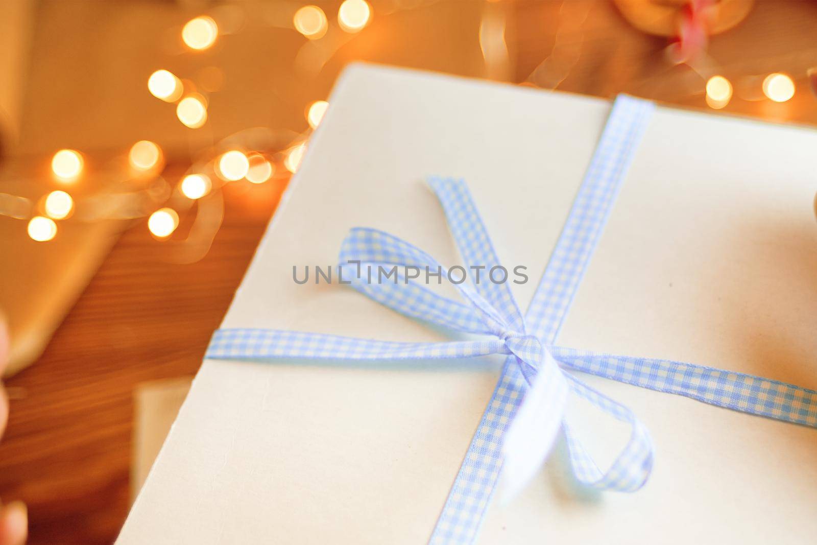 Close-up of blue checkered ribbon on white gift box. Christmas or Birthday surprise. Garland lights and decorations on background.