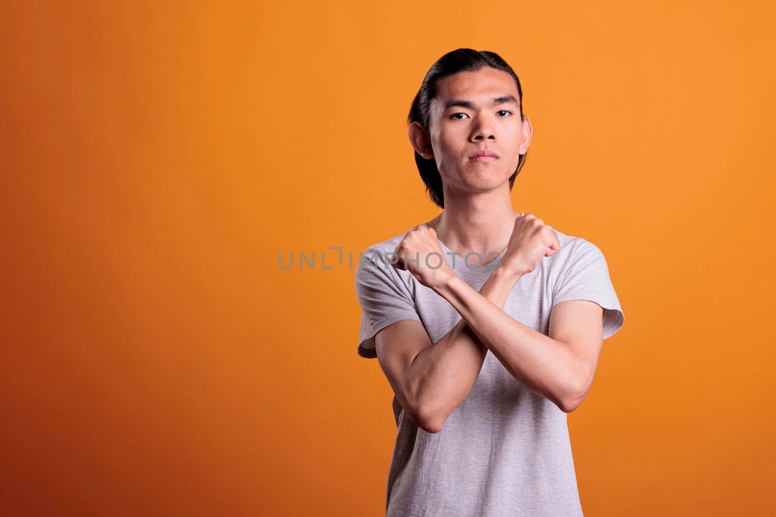 Serious young asian man showing stop gesture, strength, defense, denial concept. Teenager with crossed arms, clenched fists, confident facial expression looking at camera