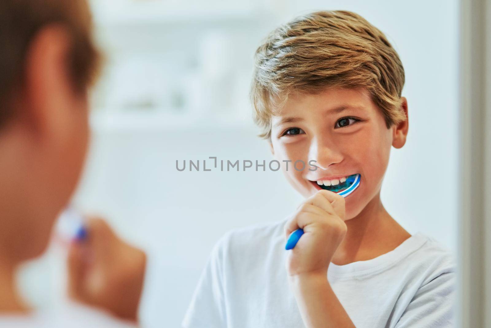 Got to brush those teeth in the morning. a cheerful young boy looking at his reflection in a mirror while brushing his teeth in the bathroom at home during the day