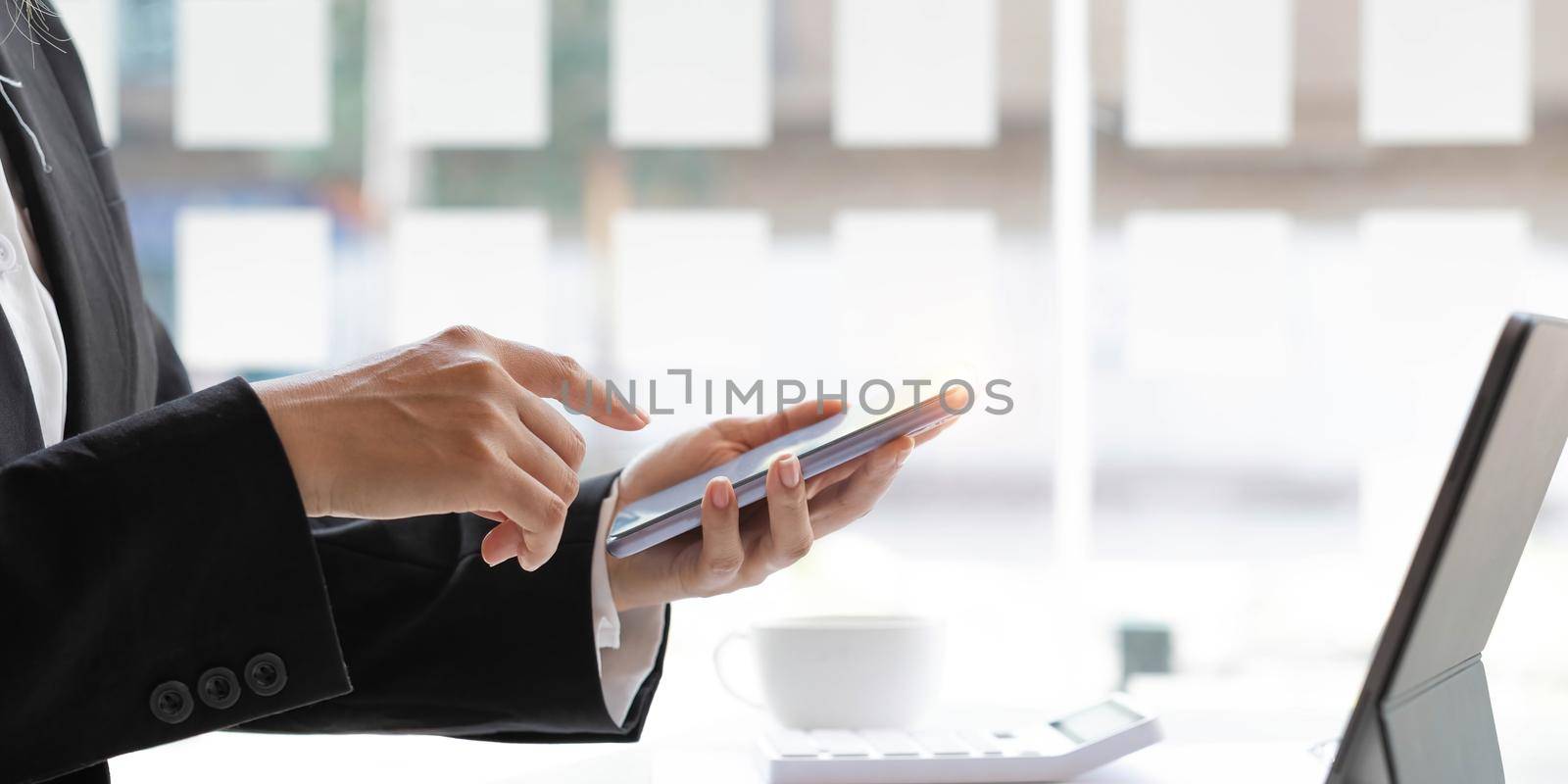 Closeup woman hands using smartphone while sitting at her office desk in modern room..