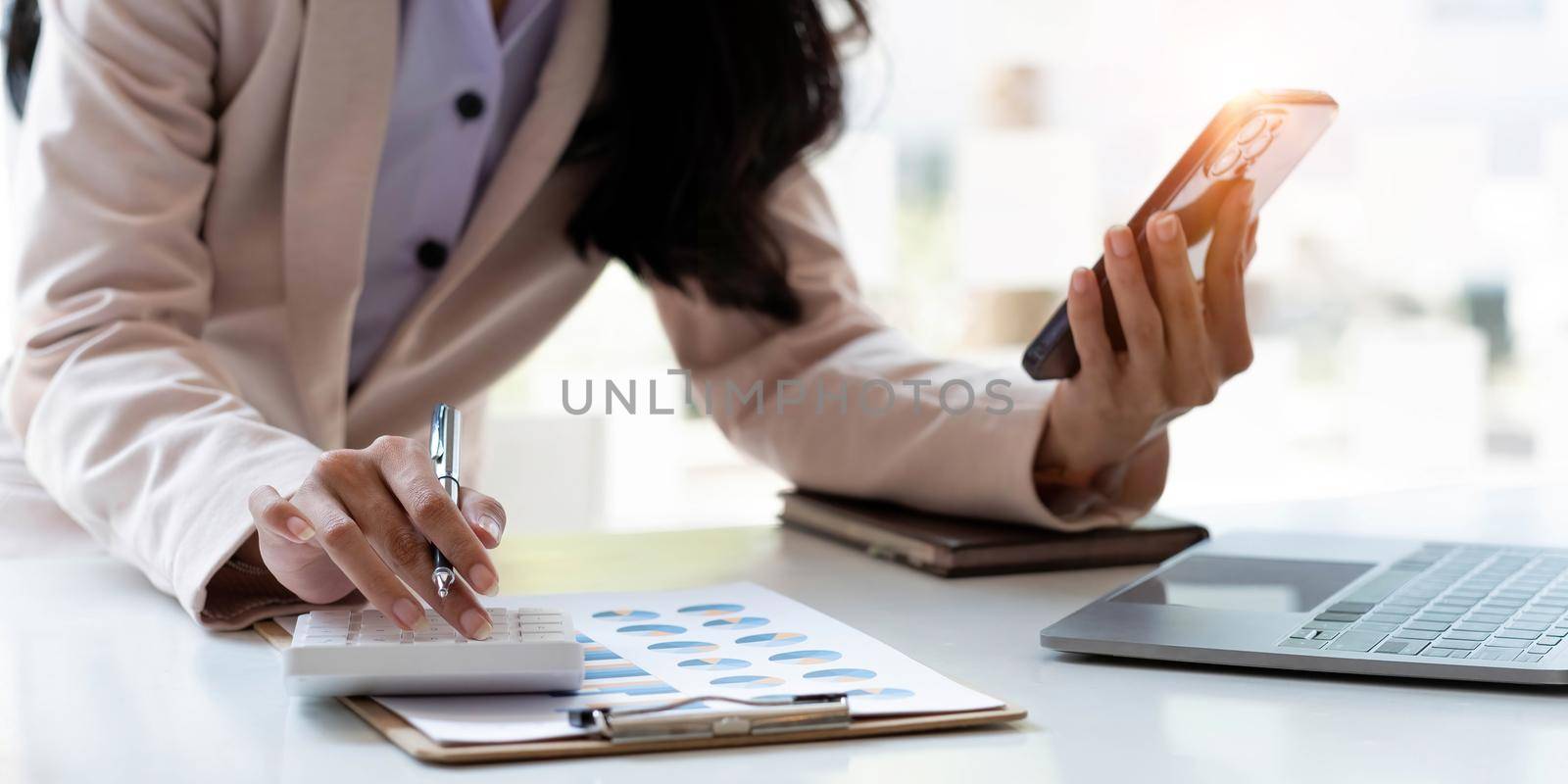 Business woman or accountant hand using calculator, working on mobile smart phone and laptop computer with documentary data graph paper on the table at modern home office. Online marketing concept. by wichayada