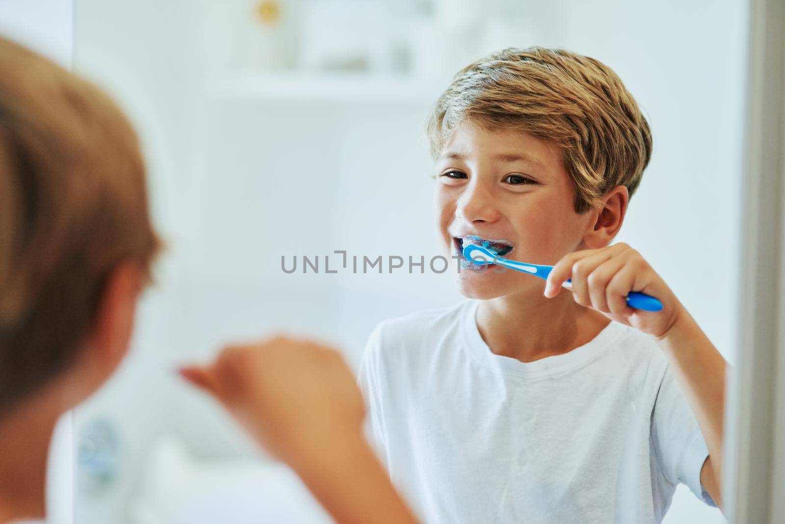 Brushing your teeth is an important routine. a cheerful young boy looking at his reflection in a mirror while brushing his teeth in the bathroom at home during the day. by YuriArcurs