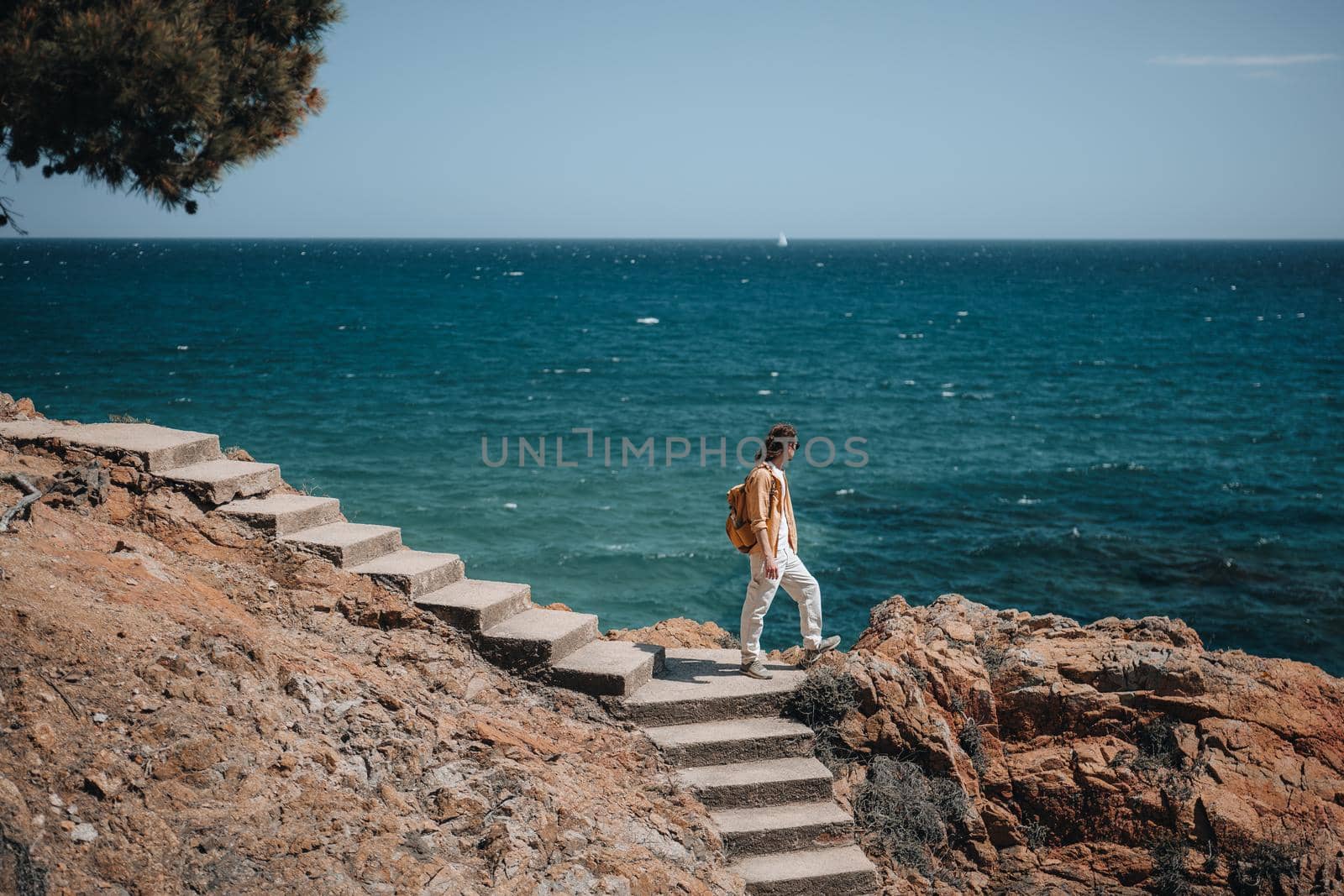 A traveler with long hair stands on stairs and looking to the deep blue sea. Travel and hiking concept in summer