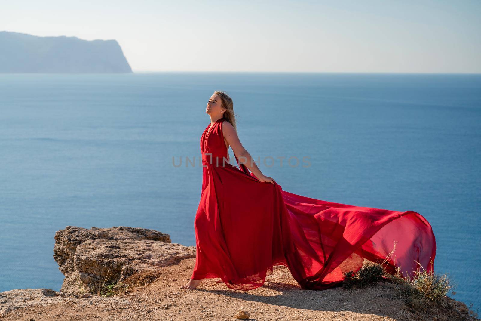 A woman in a red flying dress fluttering in the wind, against the backdrop of the sea