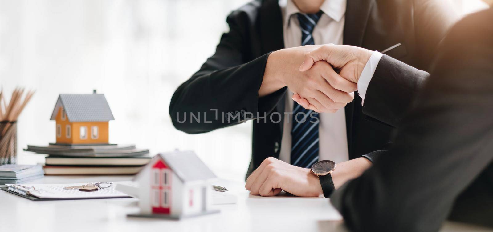 Real estate broker and customer shaking hands after signing a contract: real estate, home loan and insurance concept by wichayada