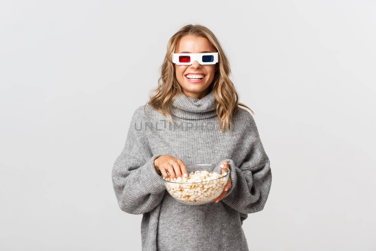 Attractive happy girl watching movie in 3d glasses, eating popcorn, standing over white background.