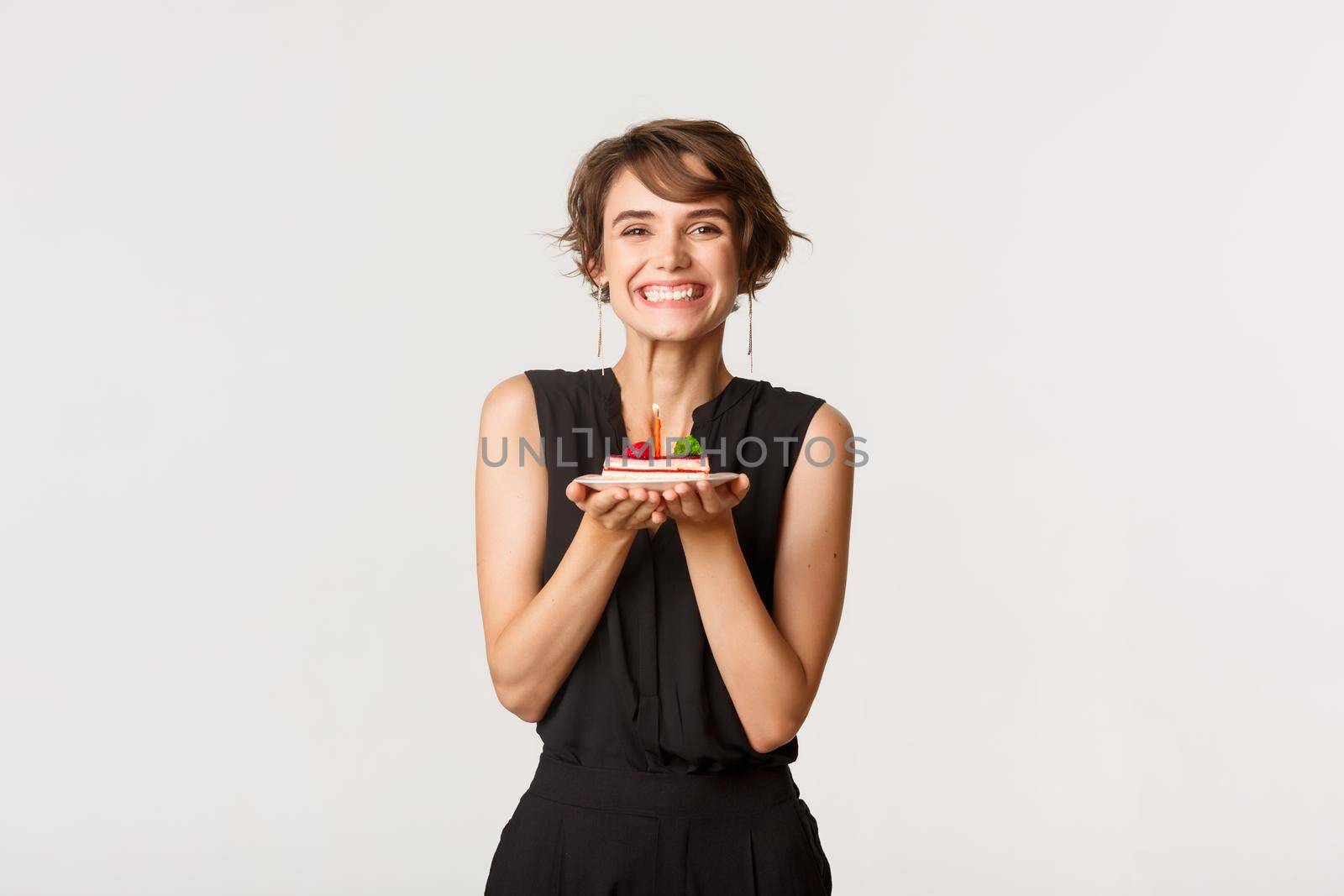 Happy beautiful b-day girl holding birthday cake and smiling, standing over white background.