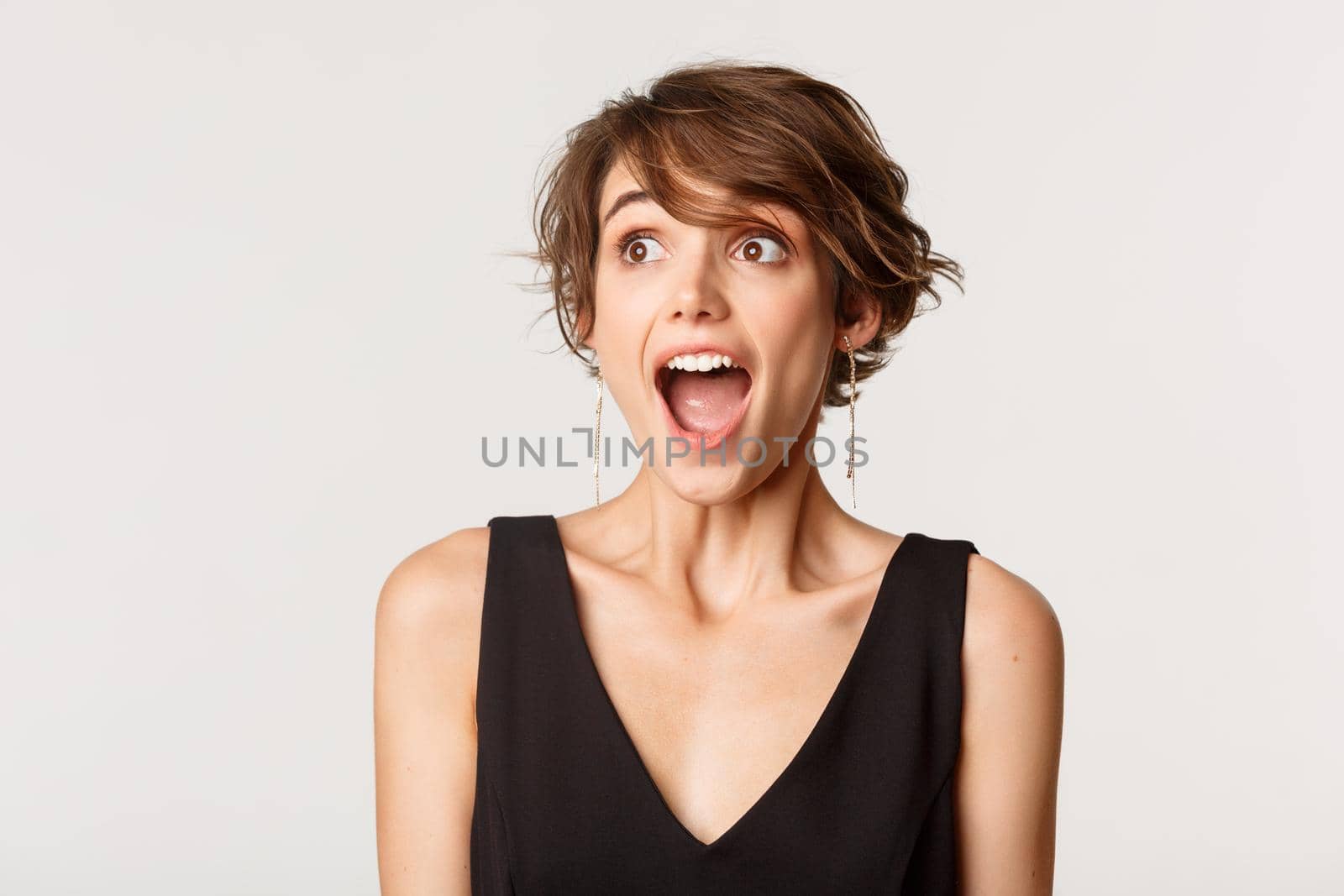 Close-up of excited, amazed young woman drop jaw and looking left, standing over white background by Benzoix