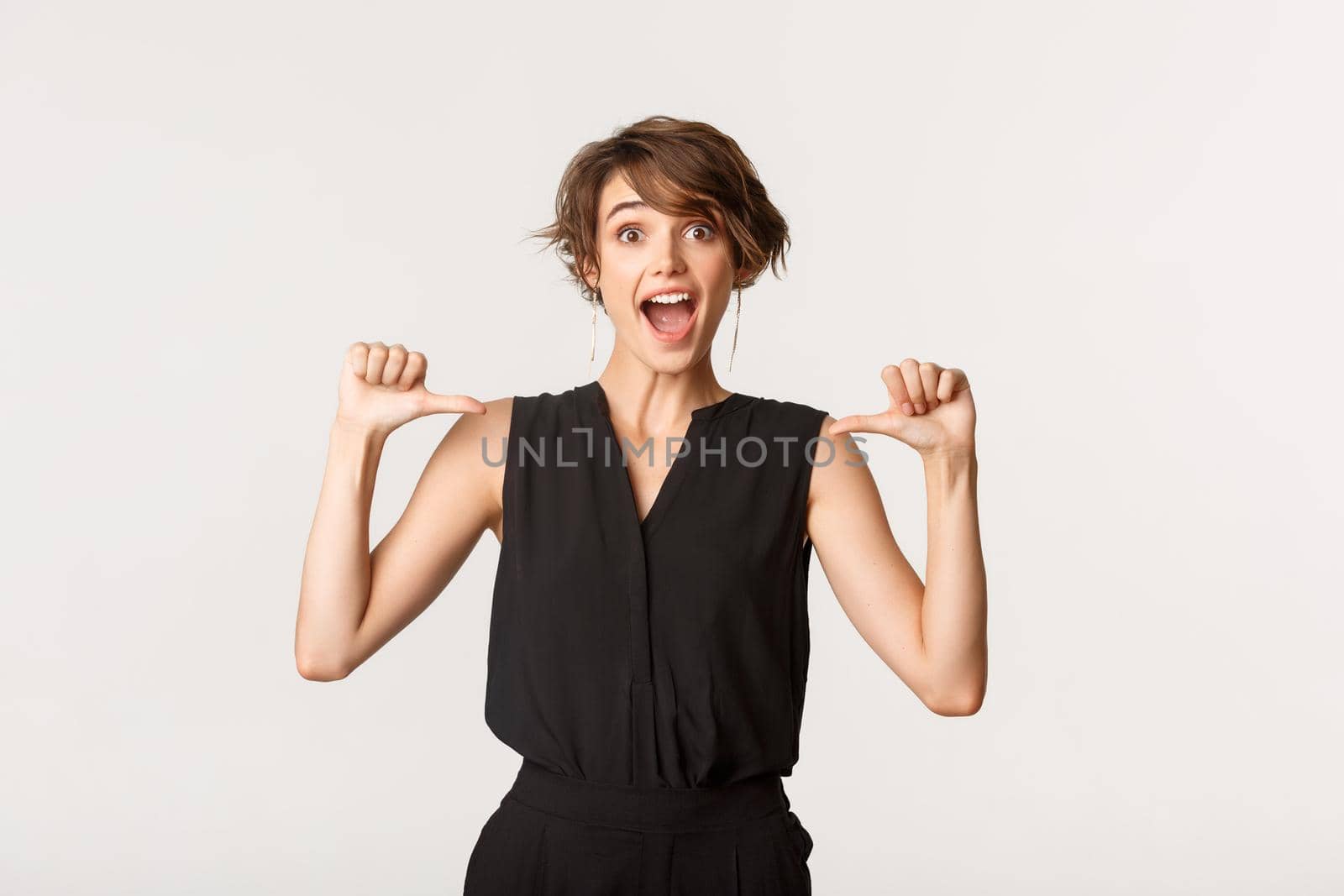 Surprised and happy beautiful girl looking amazed as pointing at herself, white background.