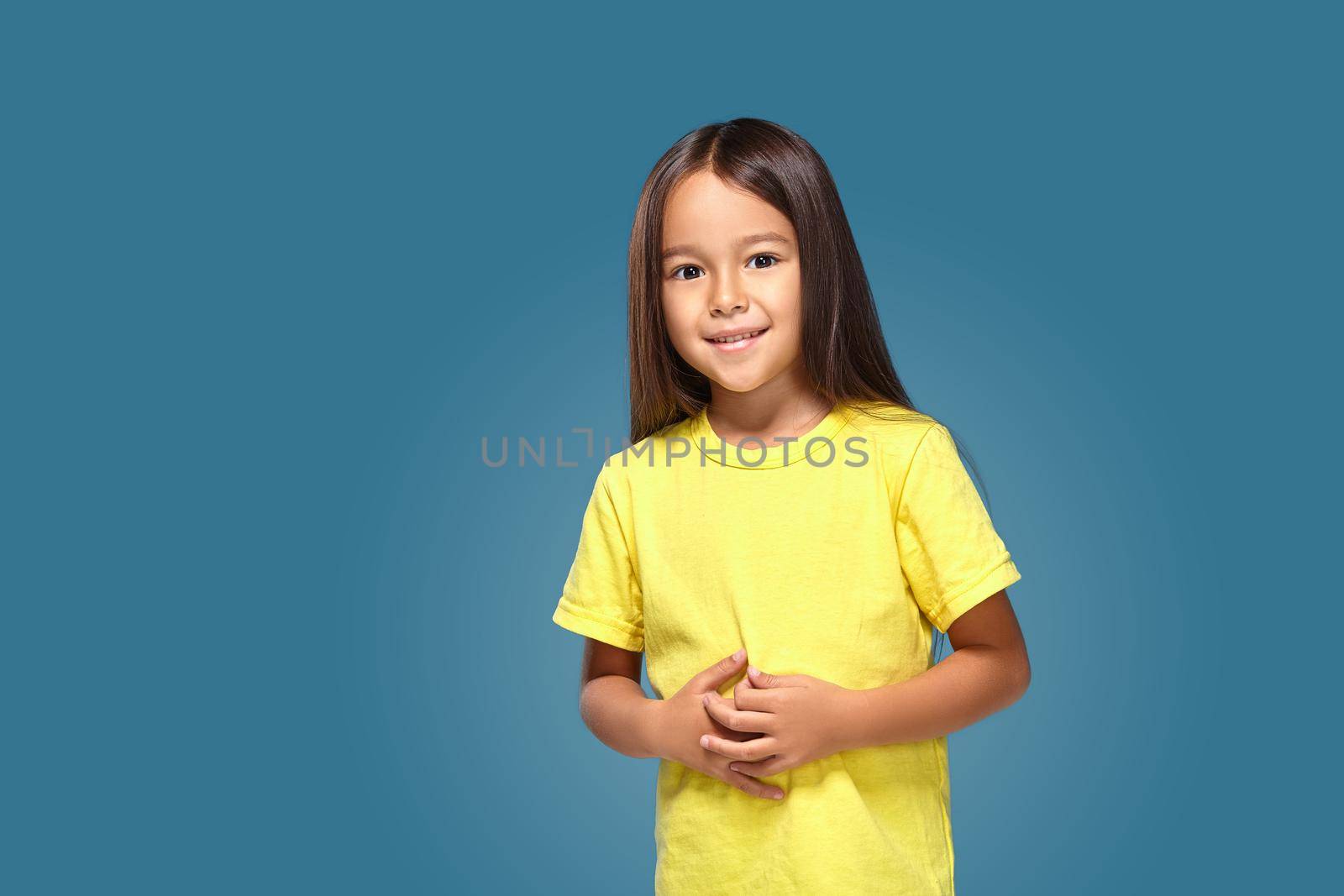 Little girl in yellow t-shirt is smiling on blue background