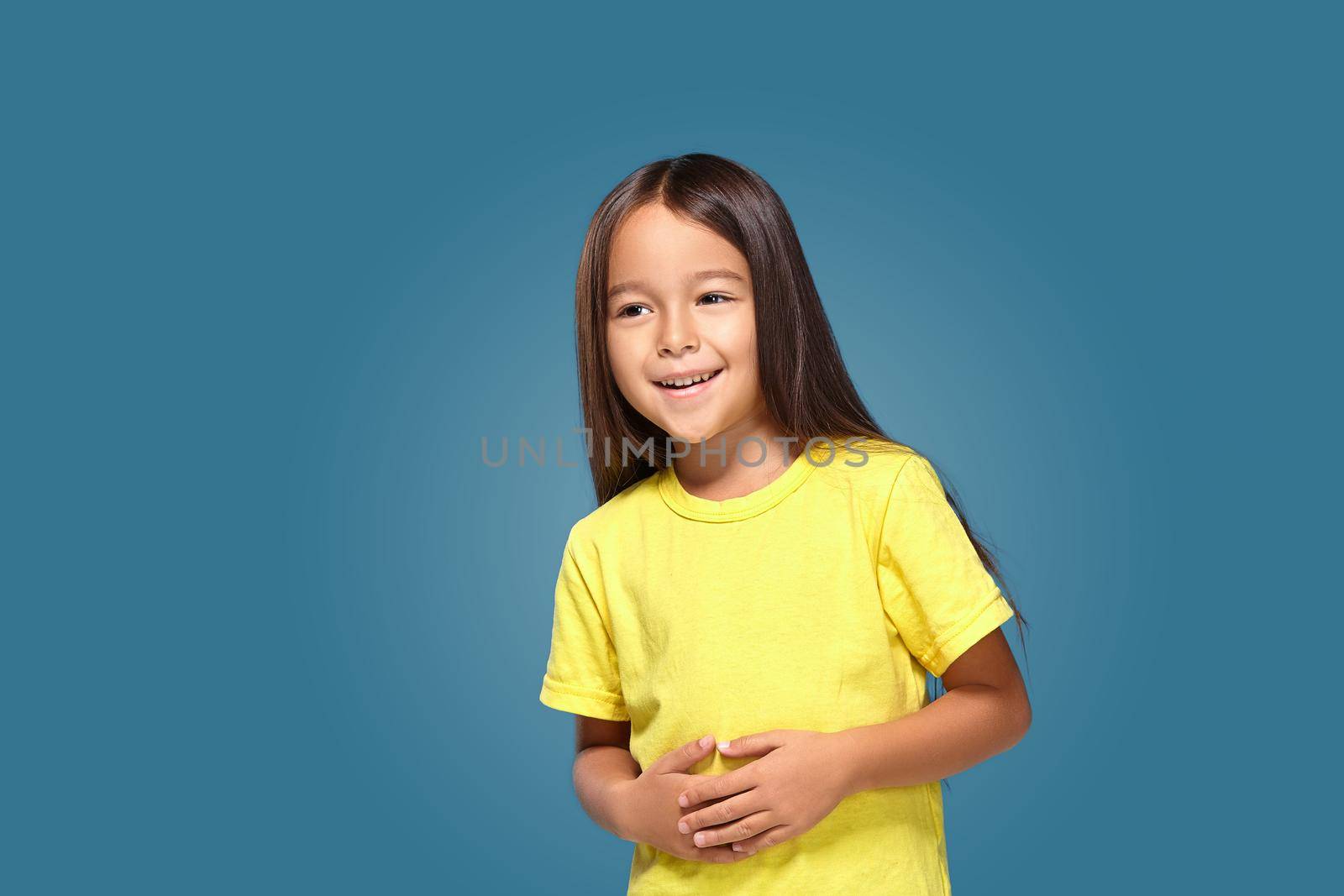 Little girl in yellow t-shirt is smiling on blue background