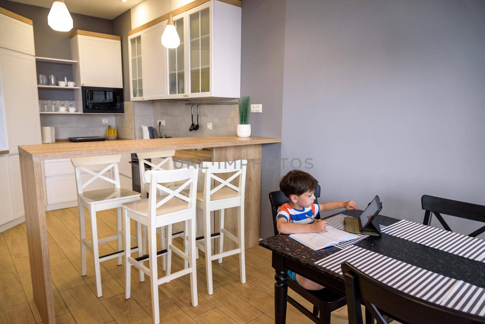 Smart preteen schoolboy doing his homework with digital tablet at home. Child using gadgets on his kitchen to study. Modern education and learning for kids.