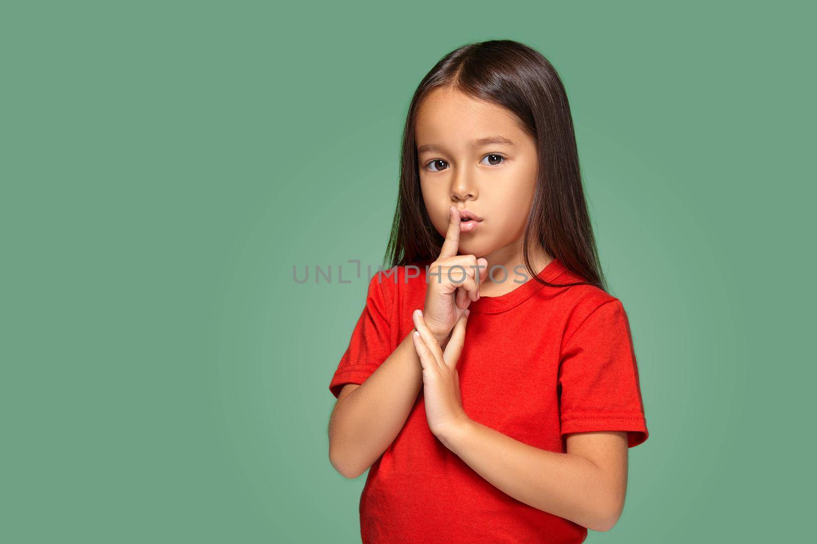 girl placing finger on lips asking shh, quiet, silence on green background