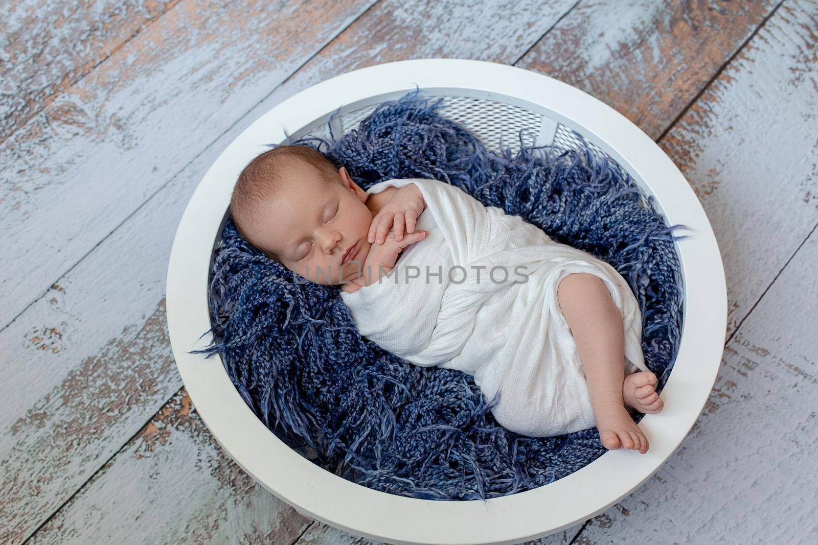Little baby boy sleeping in a basket on the wooden floor, studio shot. Newborn. 14 days