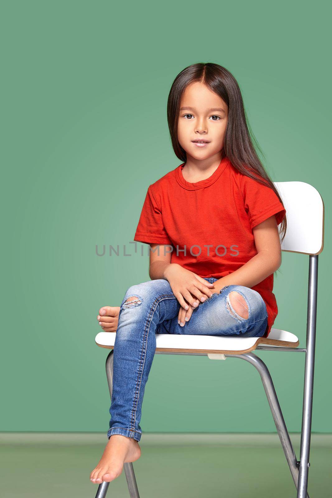 little girl wearing red t-short and posing on chair on green background
