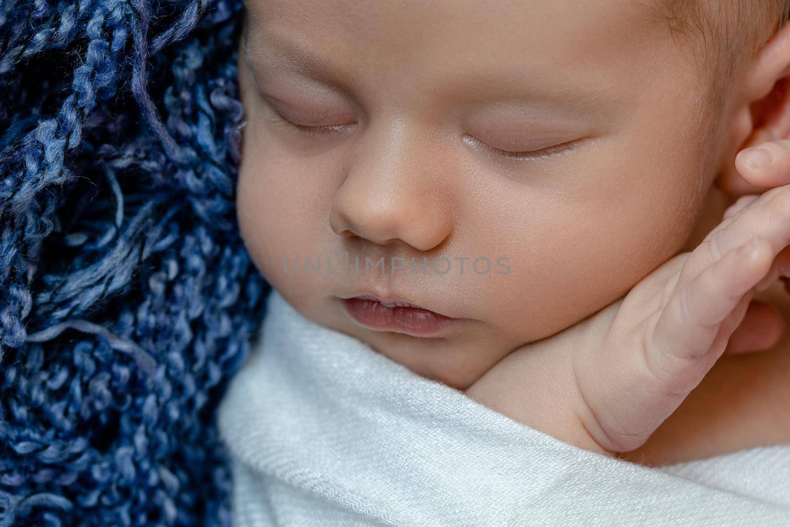 Newborn - baby, face close-up. The sleeping Newborn boy under a white knitted blanket lies on the blue fur. by nazarovsergey