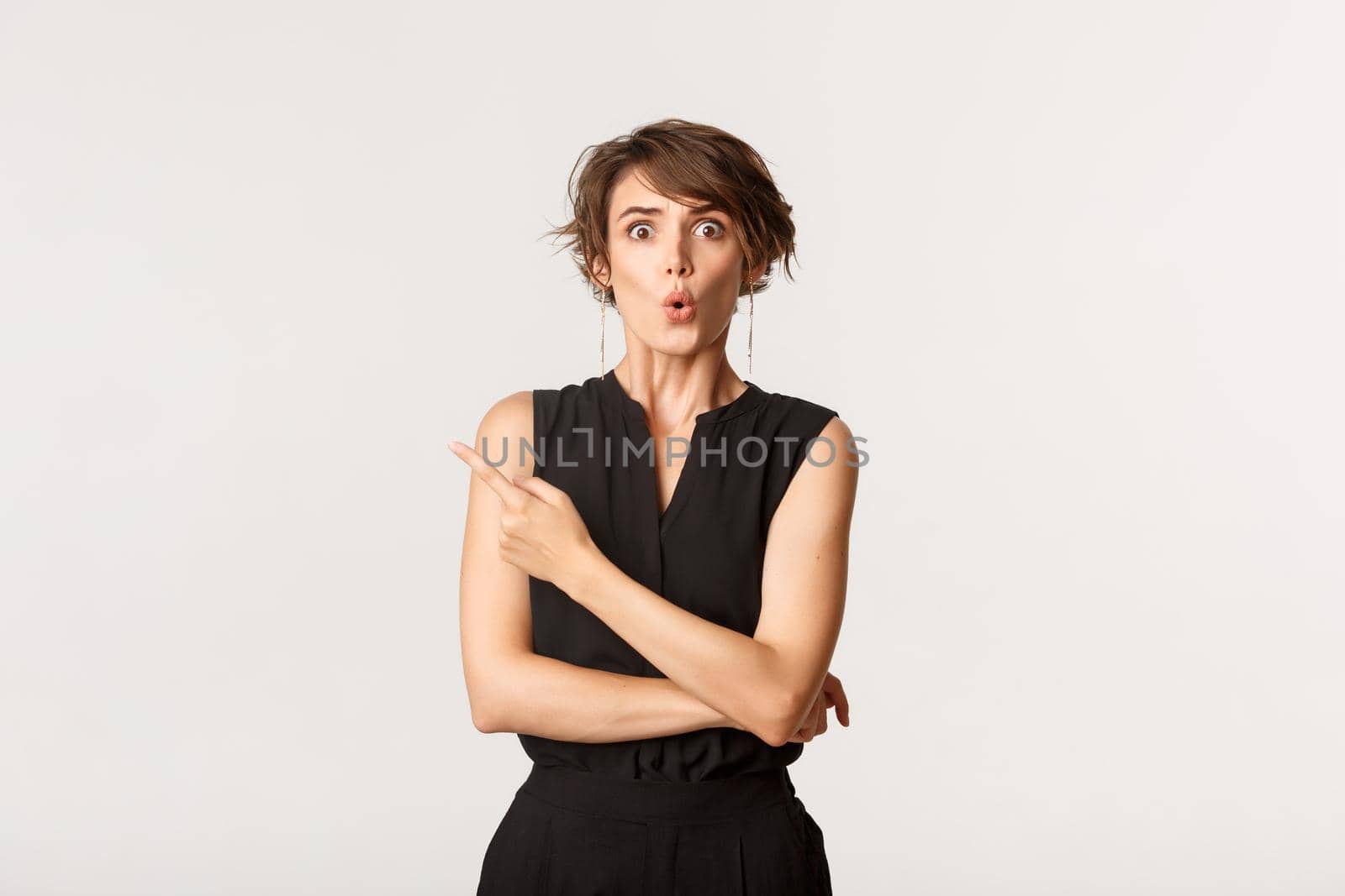 Portrait of confused young woman with short haircut, looking puzzled while pointing upper left corner at logo, white background.