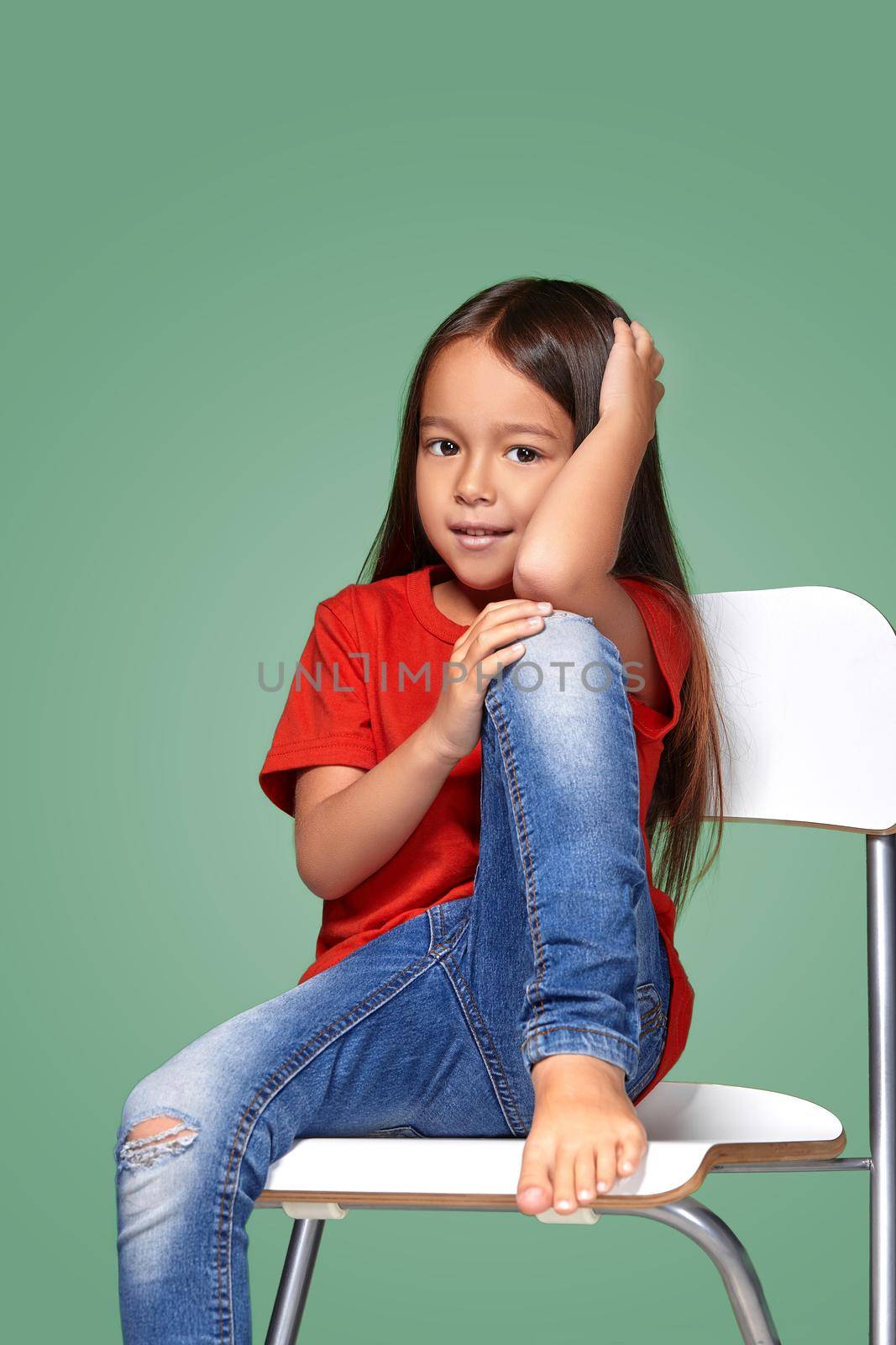 little girl wearing red t-short and posing on chair on green background