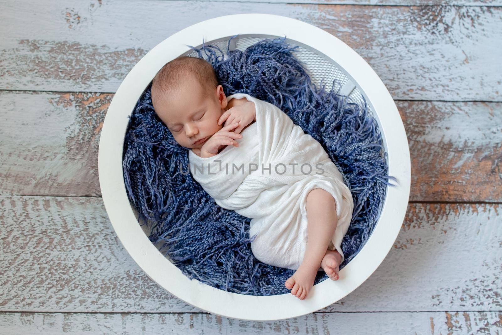Little baby boy sleeping in a basket on the wooden floor, studio shot by nazarovsergey