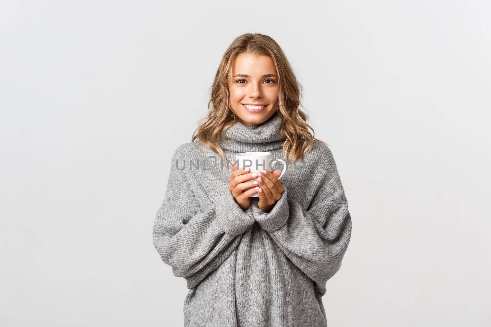 Image of beautiful smiling woman drinking coffee or tea from white mug, standing over white background.