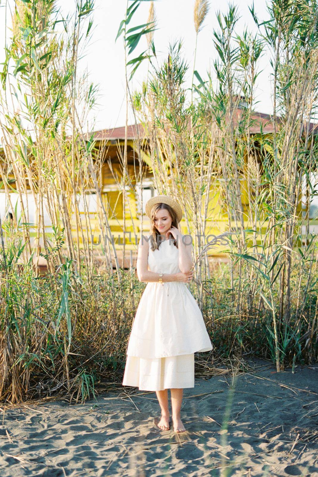 Young woman stands barefoot on the sand with a reed branch in her hand. High quality photo