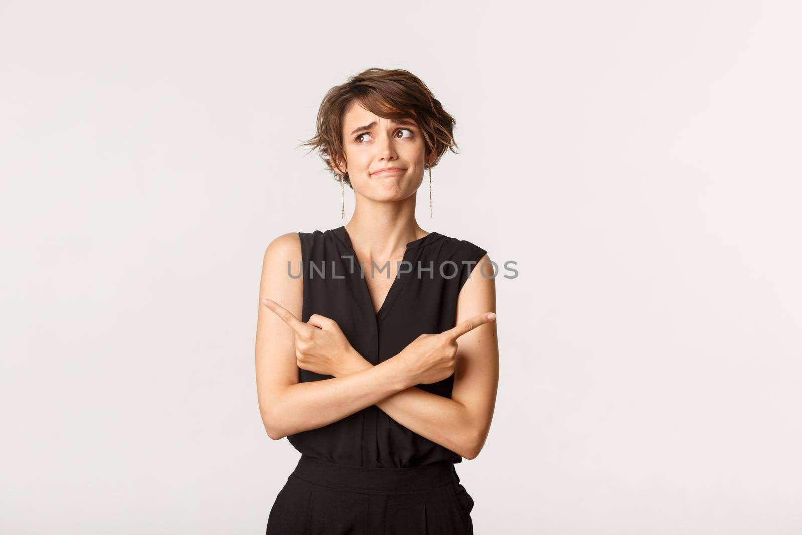 Indecisive cute girl having problem with making choice, pouting perplexed, pointing fingers sideways, white background by Benzoix