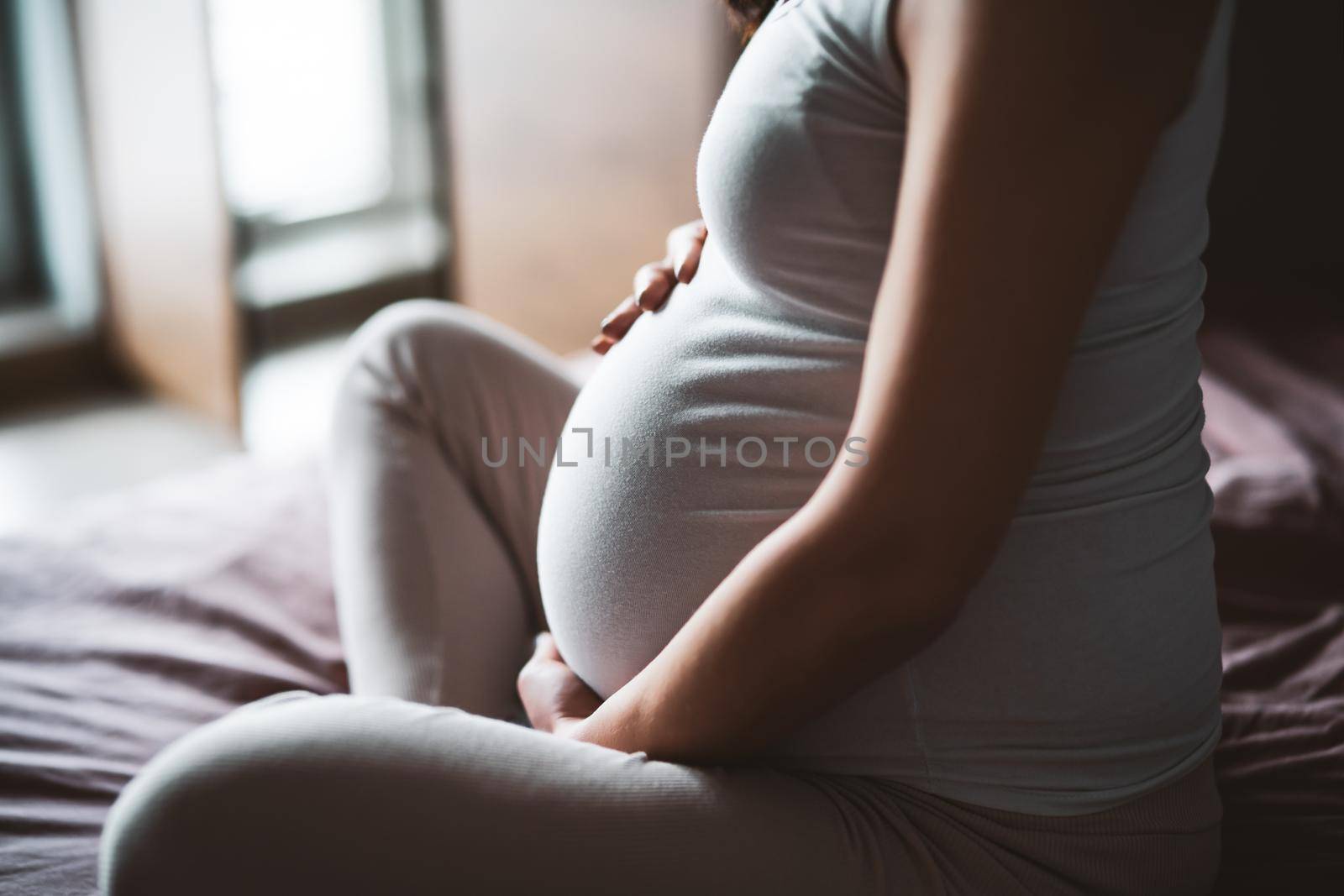 Pregnant woman relaxing at home. She is sitting on bed in bedroom.