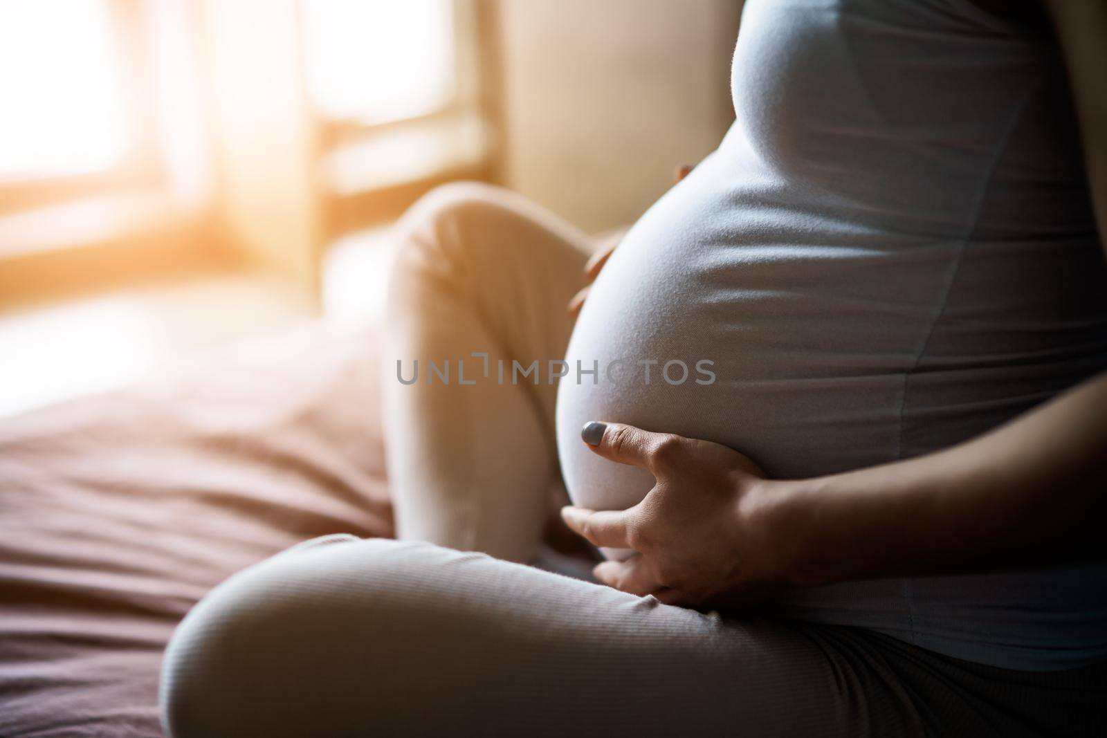 Pregnant woman relaxing at home. She is sitting on bed in bedroom.