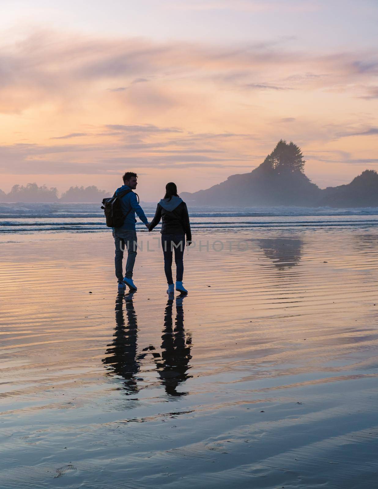 a couple of men and women mid-age watching the sunset on the beach of Tofino Vancouver Island Canada, beautiful sunset on the beach with pink-purple colors in the sky. Canada Tofino Vancouver Island