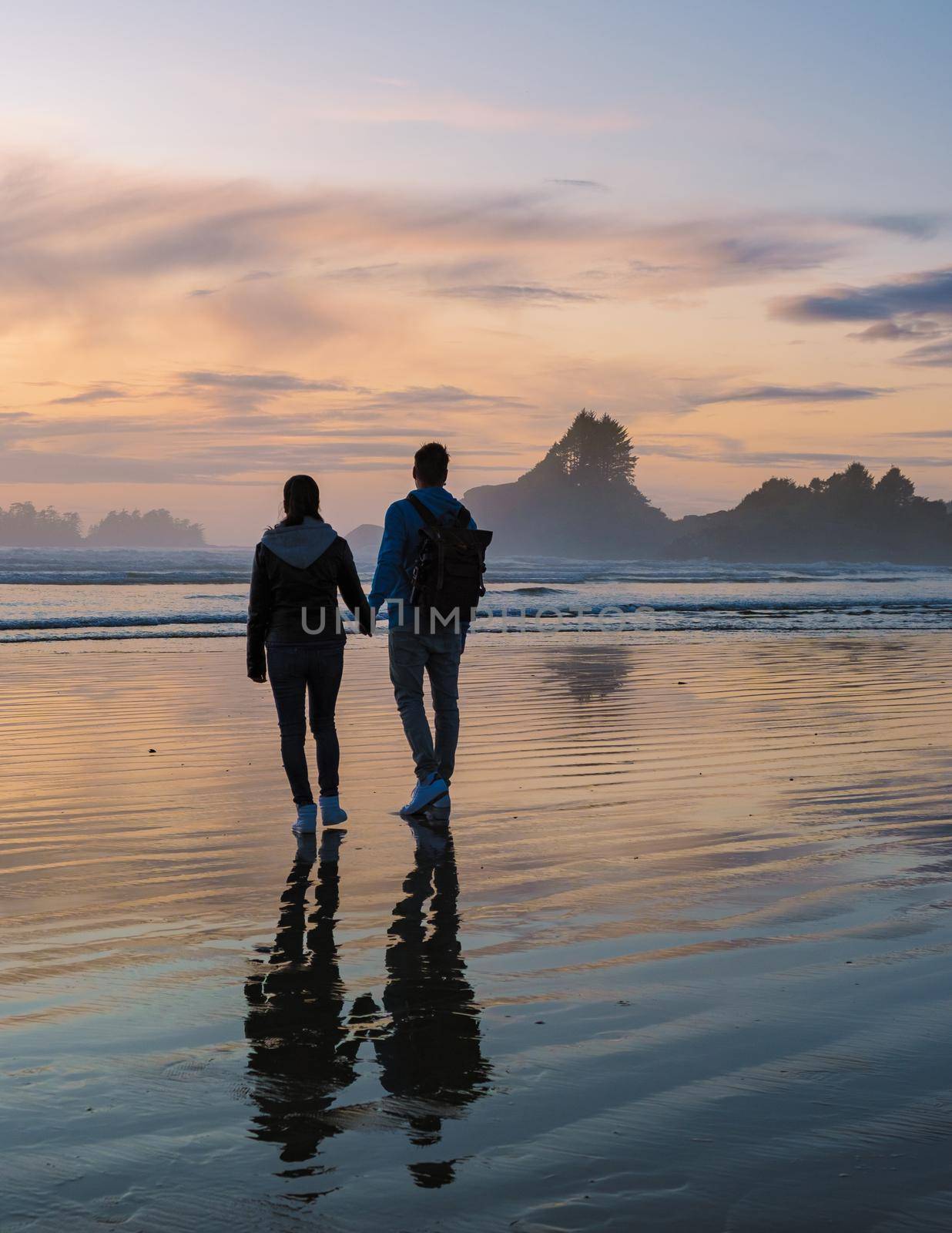 a couple of men and women mid-age watching the sunset on the beach of Tofino Vancouver Island Canada, beautiful sunset on the beach with pink-purple colors in the sky. Canada Tofino Vancouver Island