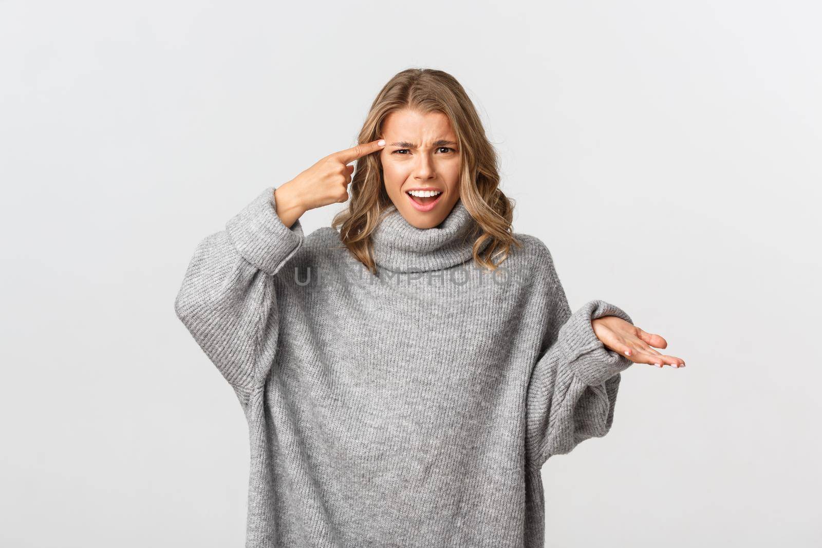 Image of annoyed and frustrated blond girl rolling finger over head, scolding someone for acting stupid, standing over white background by Benzoix