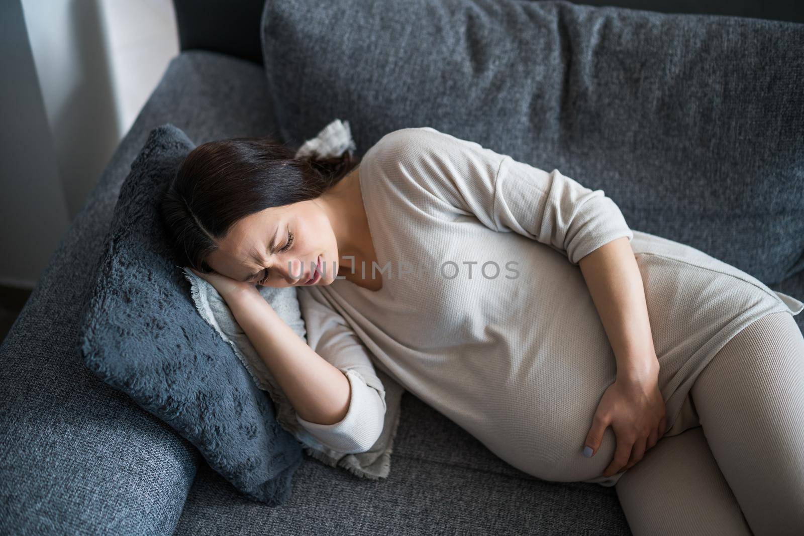 Pregnant woman is having pain in her back. She is lying on bed at home.