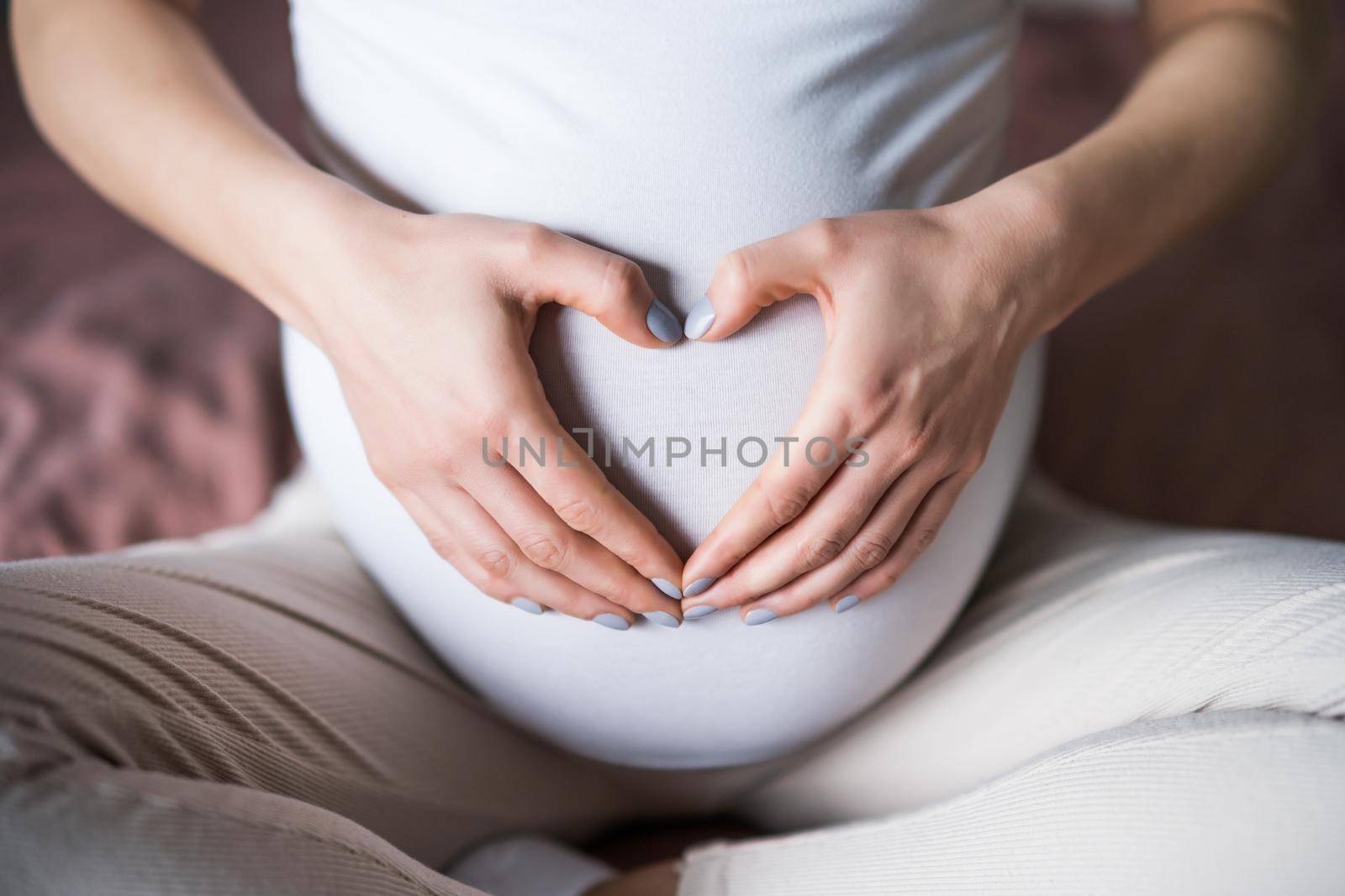Pregnant woman relaxing at home. She is making heart shape on her stomach.