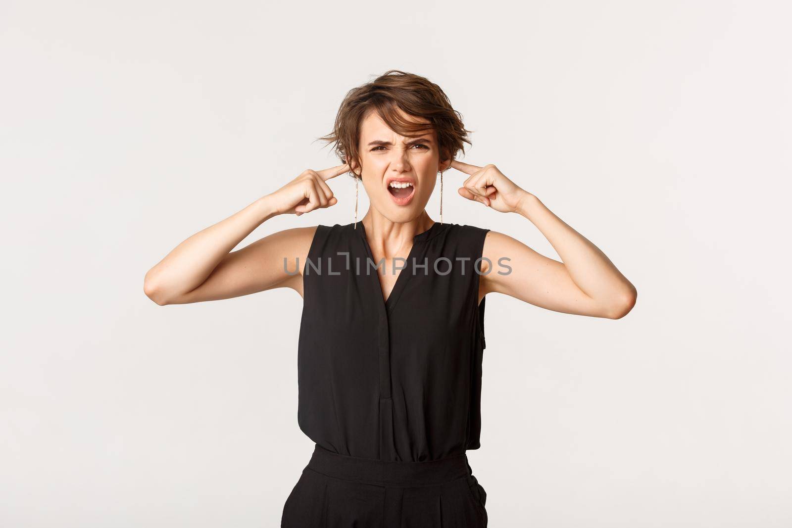 Angry and irritated young woman complaining on loud bothering noise, shut ears and grimacing annoyed.