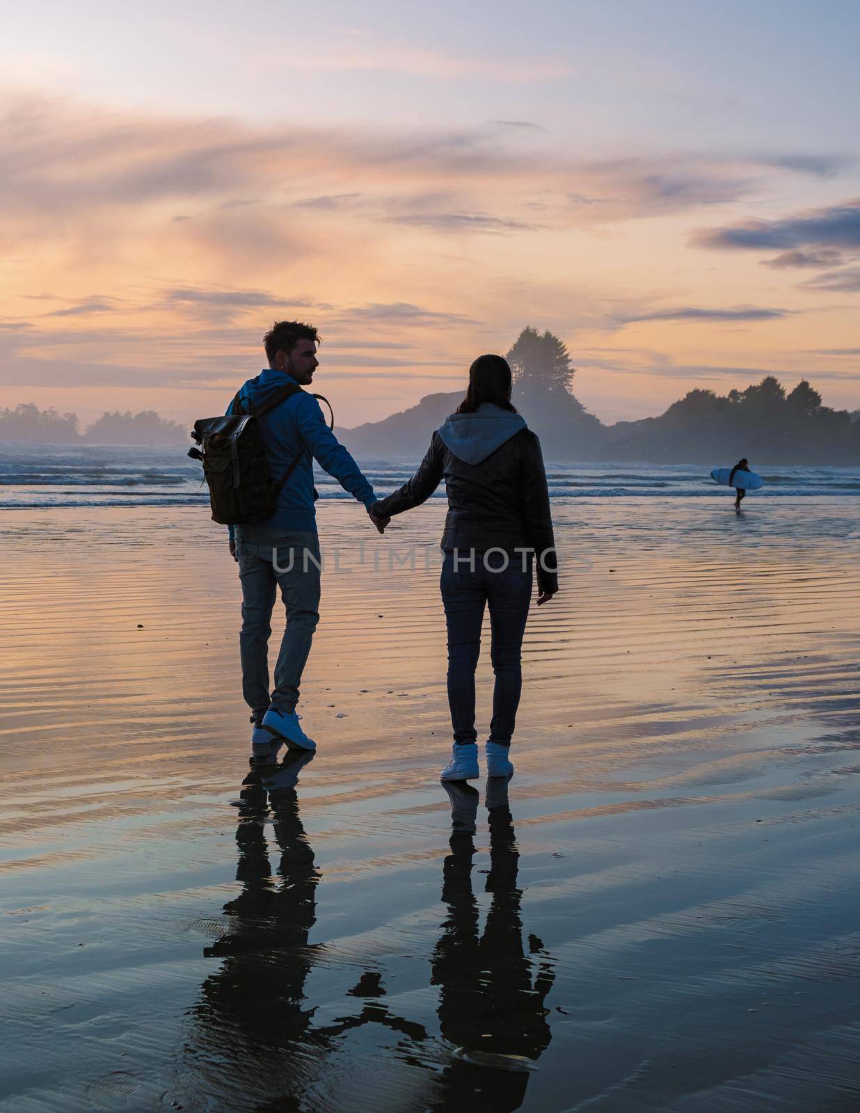 a couple of men and women mid-age watching the sunset on the beach of Tofino Vancouver Island Canada, beautiful sunset on the beach with pink-purple colors in the sky. Canada Tofino Vancouver Island