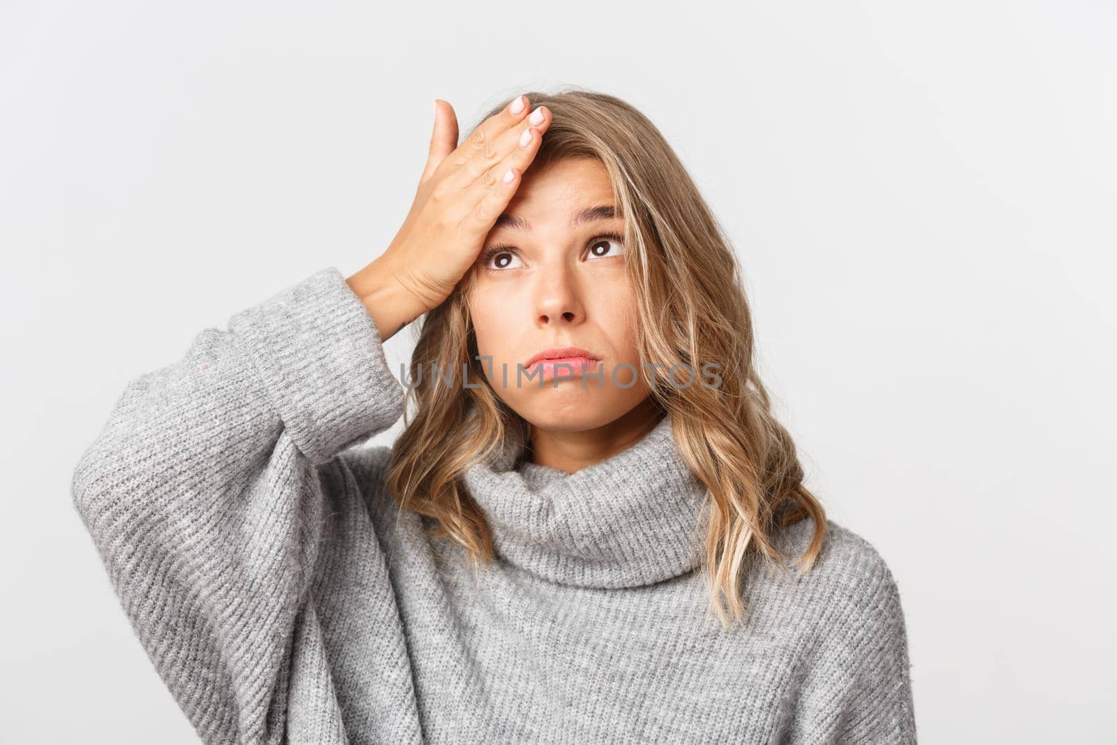 Close-up of complicated cute blond girl, slap forehead, facepalm and exhaling troubled, standing over white background and looking at upper left corner.
