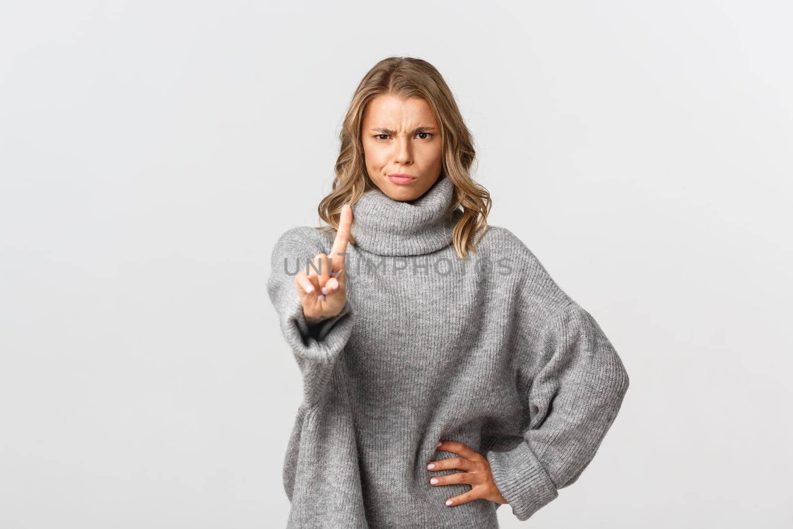 Image of serious and angry blond woman telling to stop, shaking finger disappointed, scolding someone for doing bad thing, prohibit and disagree, standing over white background.
