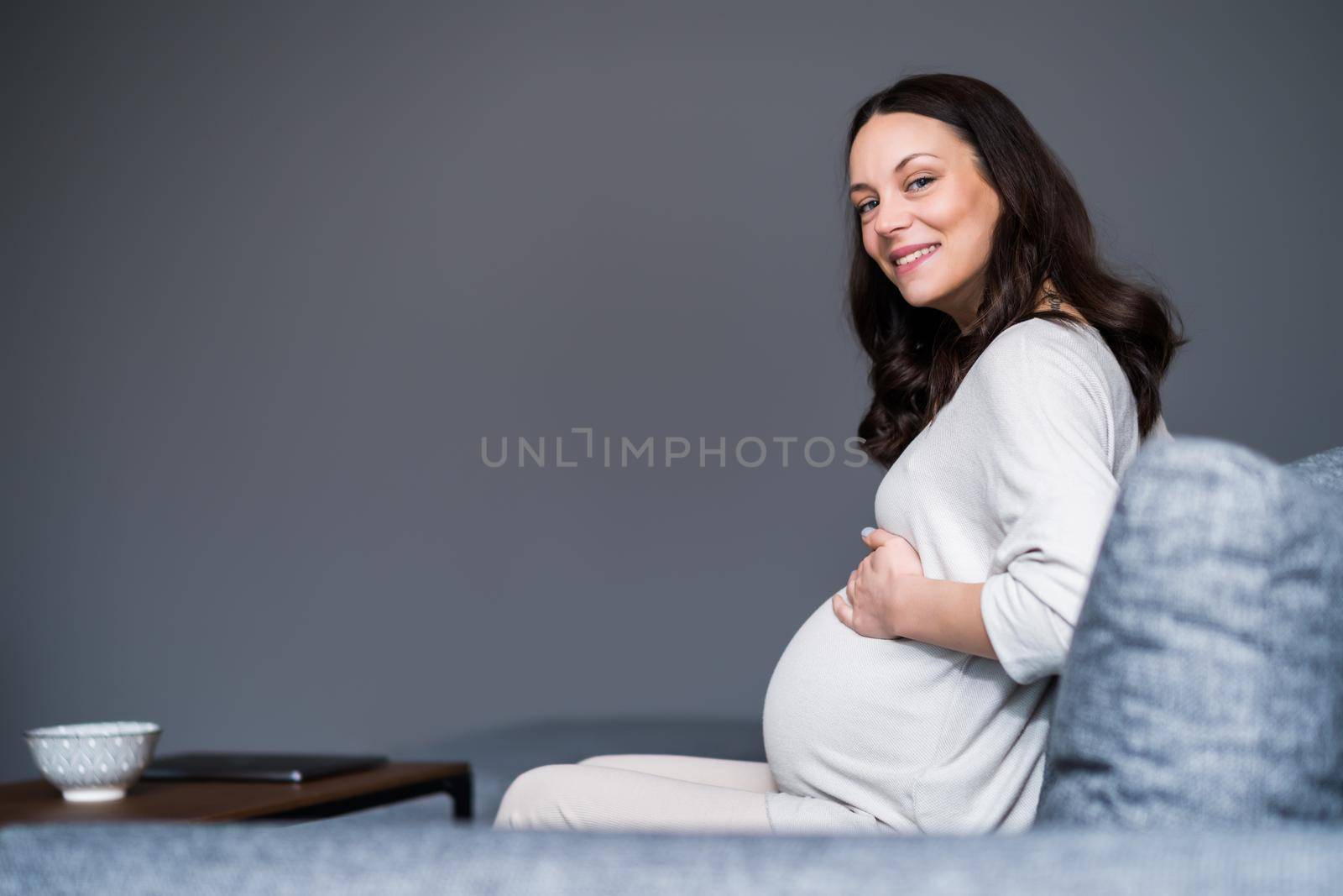 Happy pregnant woman relaxing at home. She is sitting on bed in bedroom.