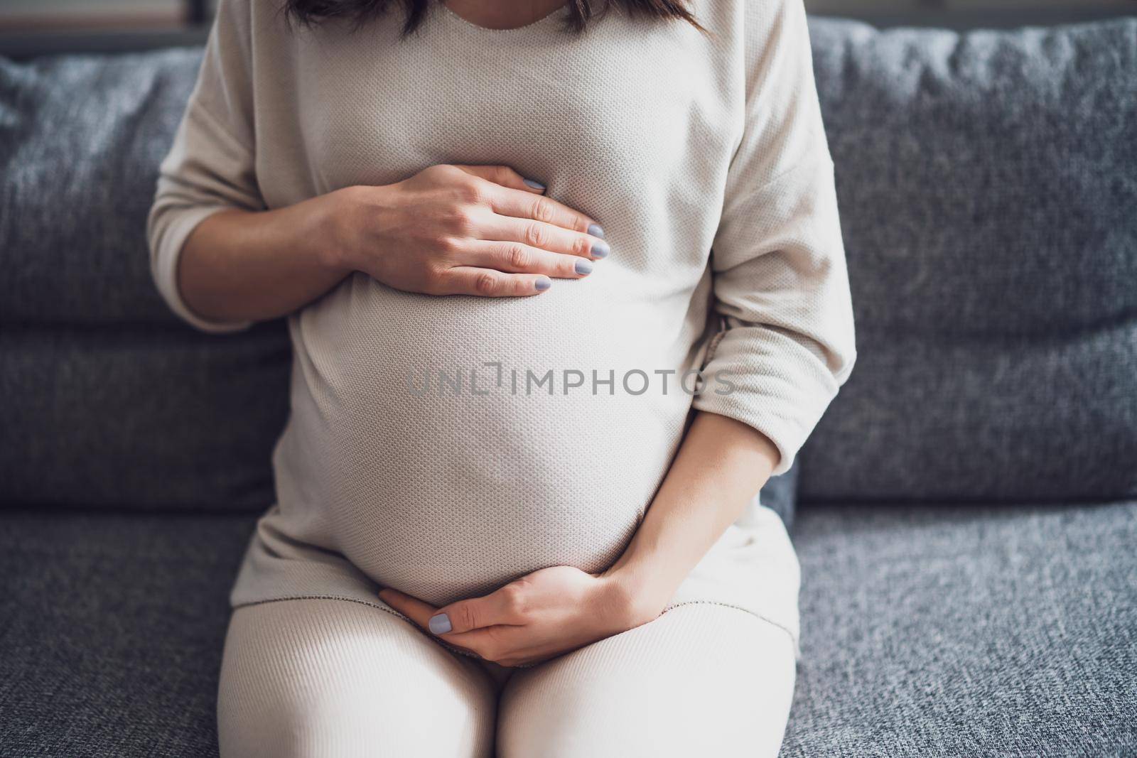 Pregnant woman relaxing at home. She is sitting on bed in bedroom.