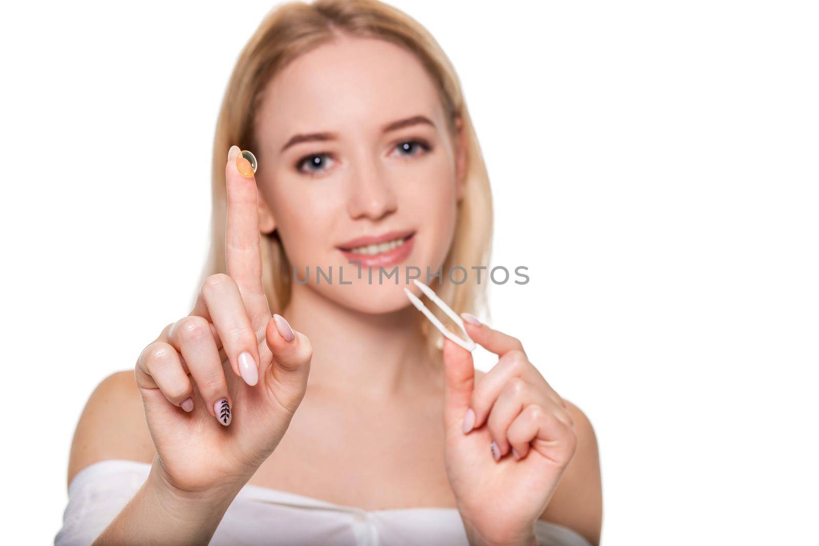 Focus on contact lens on finger of young woman. Young woman holding contact lens on finger in front of her face. Woman holding contact lens on white background. Eyesight and eyecare concept.