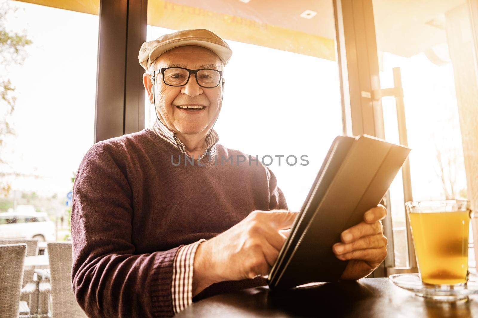 Senior man is sitting in cafe and using digital tablet.